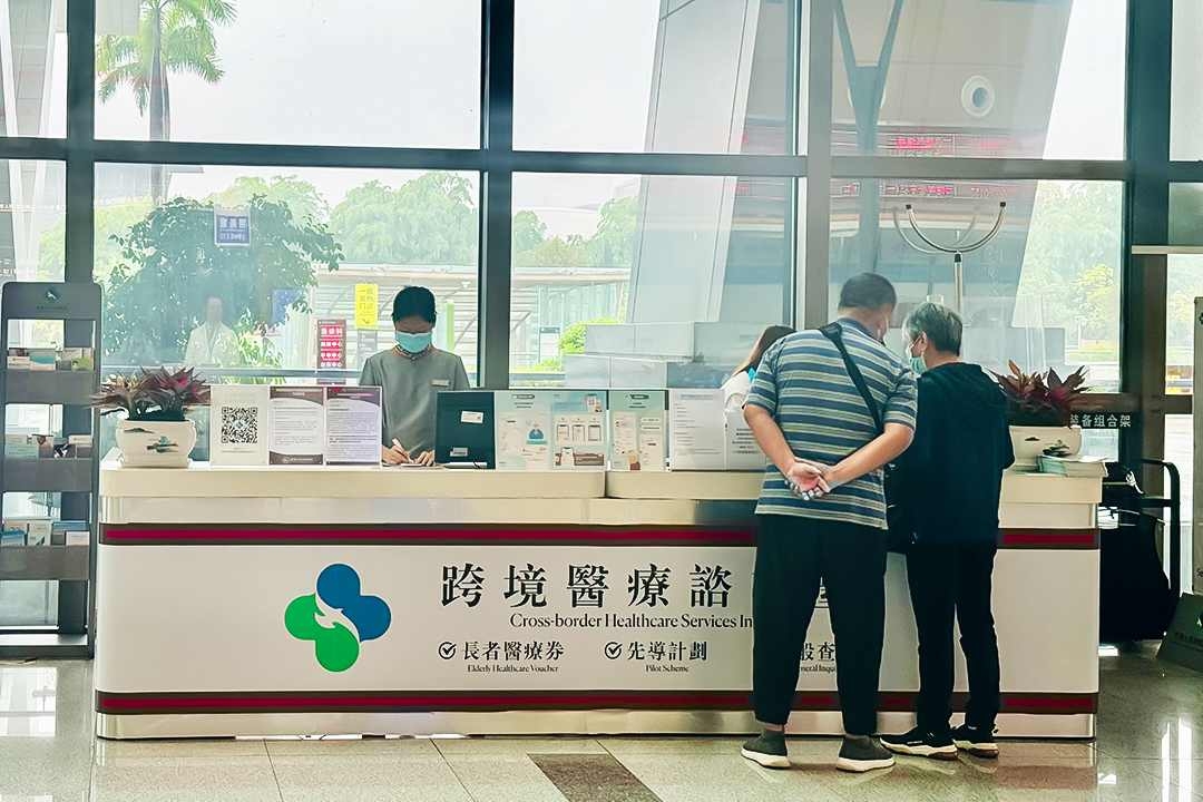 Two Hong Kong seniors ask about using elderly health care vouchers at the cross-border medical information desk at the University of Hong Kong-Shenzhen Hospital. Photo: Wen Simin/Caixin